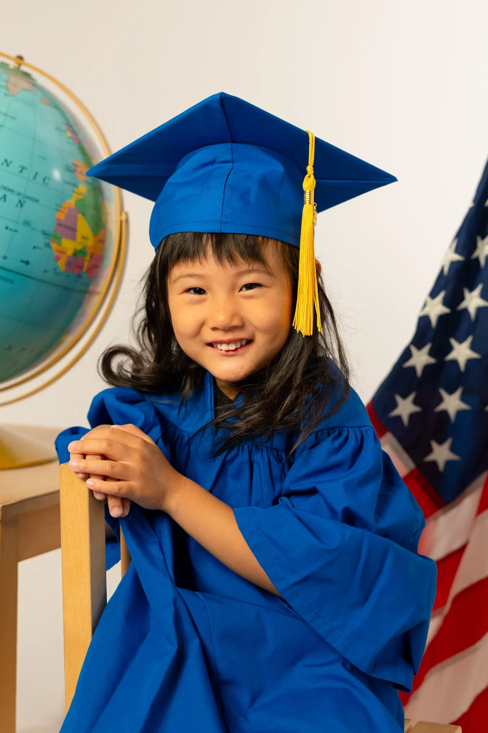 Preschooler in a blue cap and gown holding a diploma