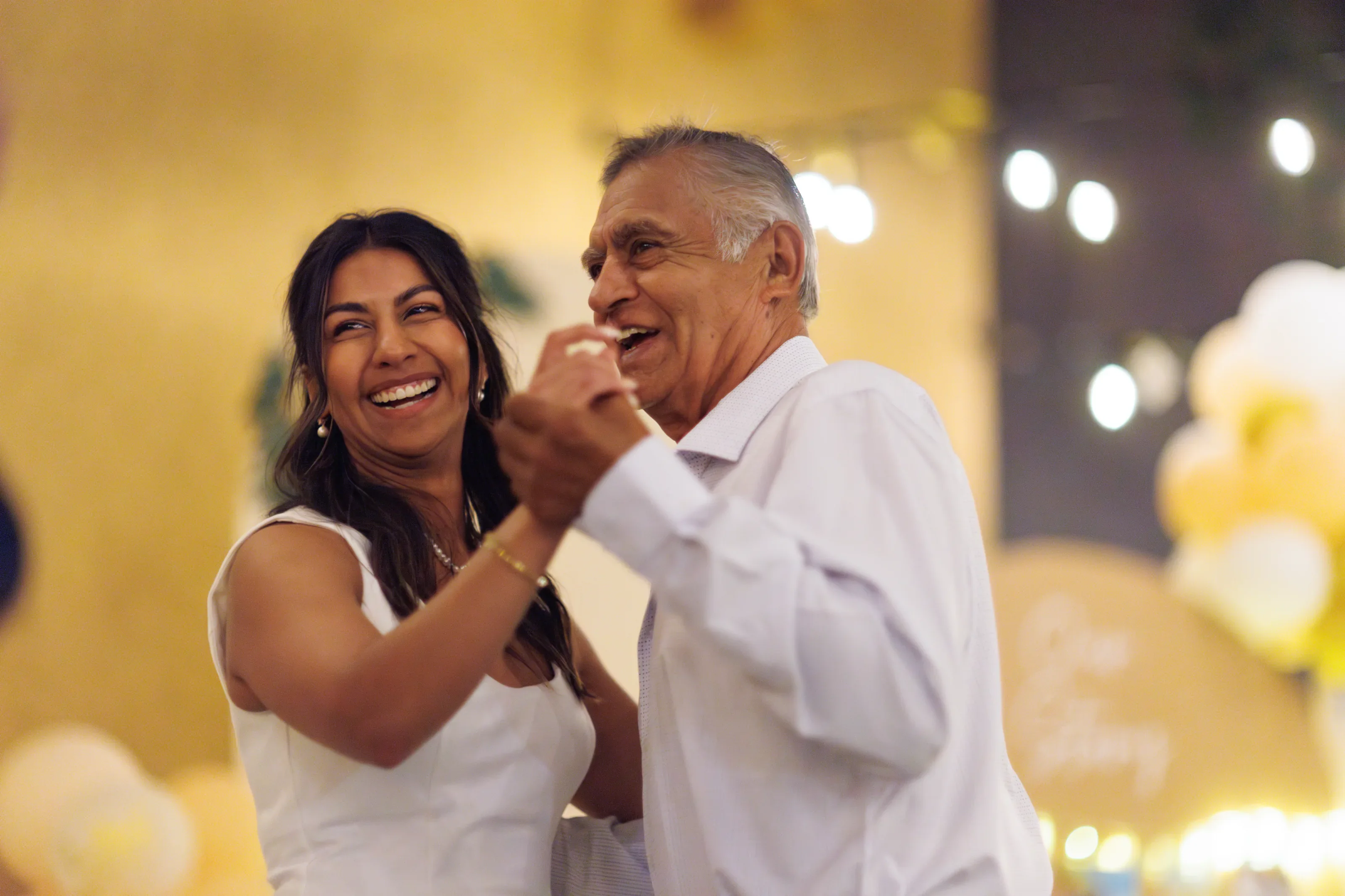 Joyful parent dance beneath warm reception lights